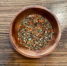 Grounding tea by Sage & Stone Apothecary shown in a rustic mug with tea leaves and herbs around it.