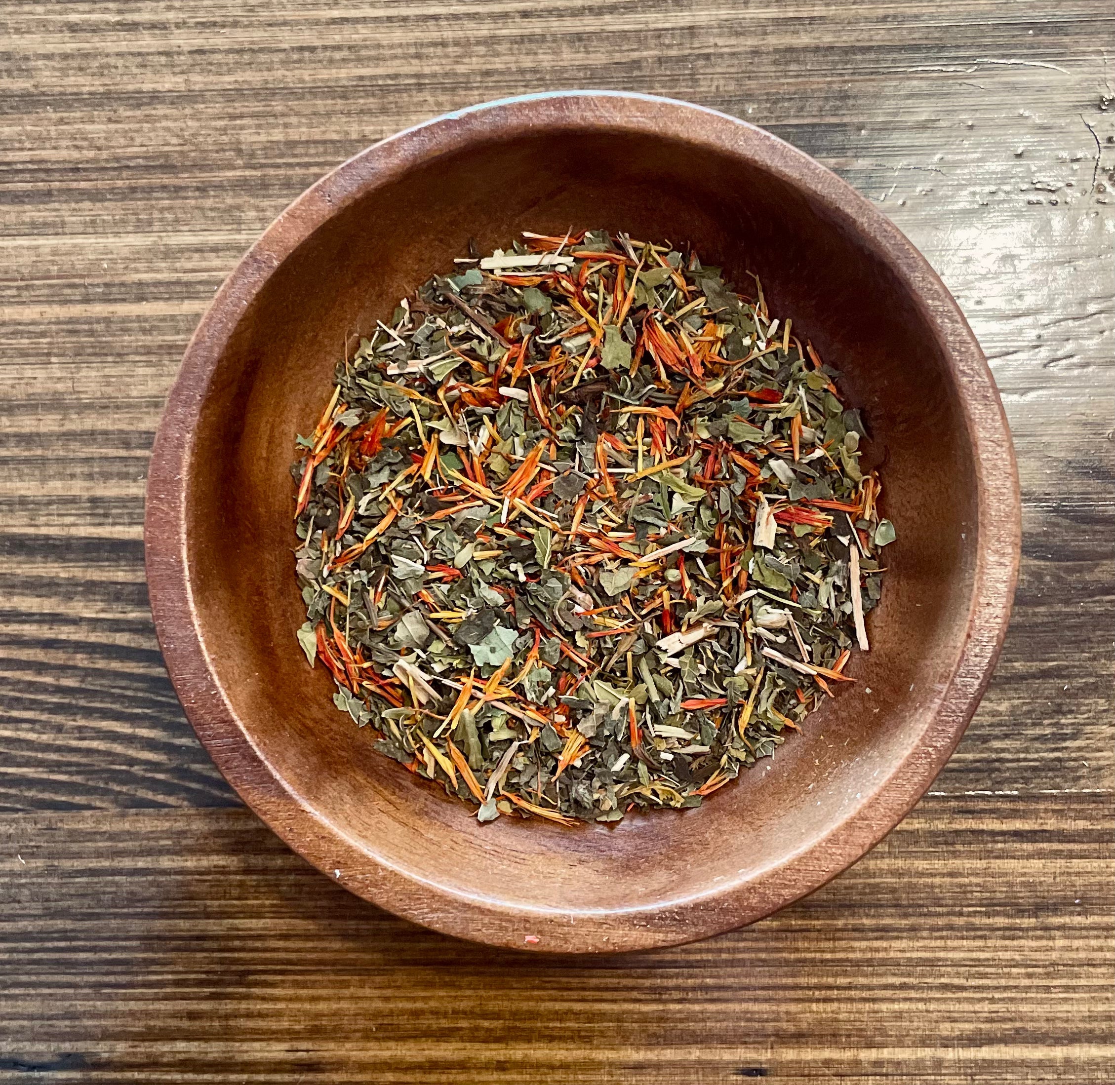 Grounding tea by Sage & Stone Apothecary shown in a rustic mug with tea leaves and herbs around it.