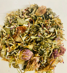 A cup of Sage & Stone Apothecary Nourishing Pregnancy Tea in a glass mug with fresh herbs and tea leaves on a wooden table.