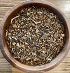 Herbal tea in a clear glass cup featuring the Slim Tummy Herbal Tea by Sage & Stone Apothecary with dried herbs nearby.