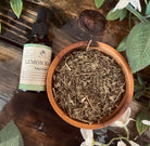 Lemon balm tincture in a glass bottle from Sage & Stone Apothecary, with a dropper cap and fresh lemon balm leaves nearby.