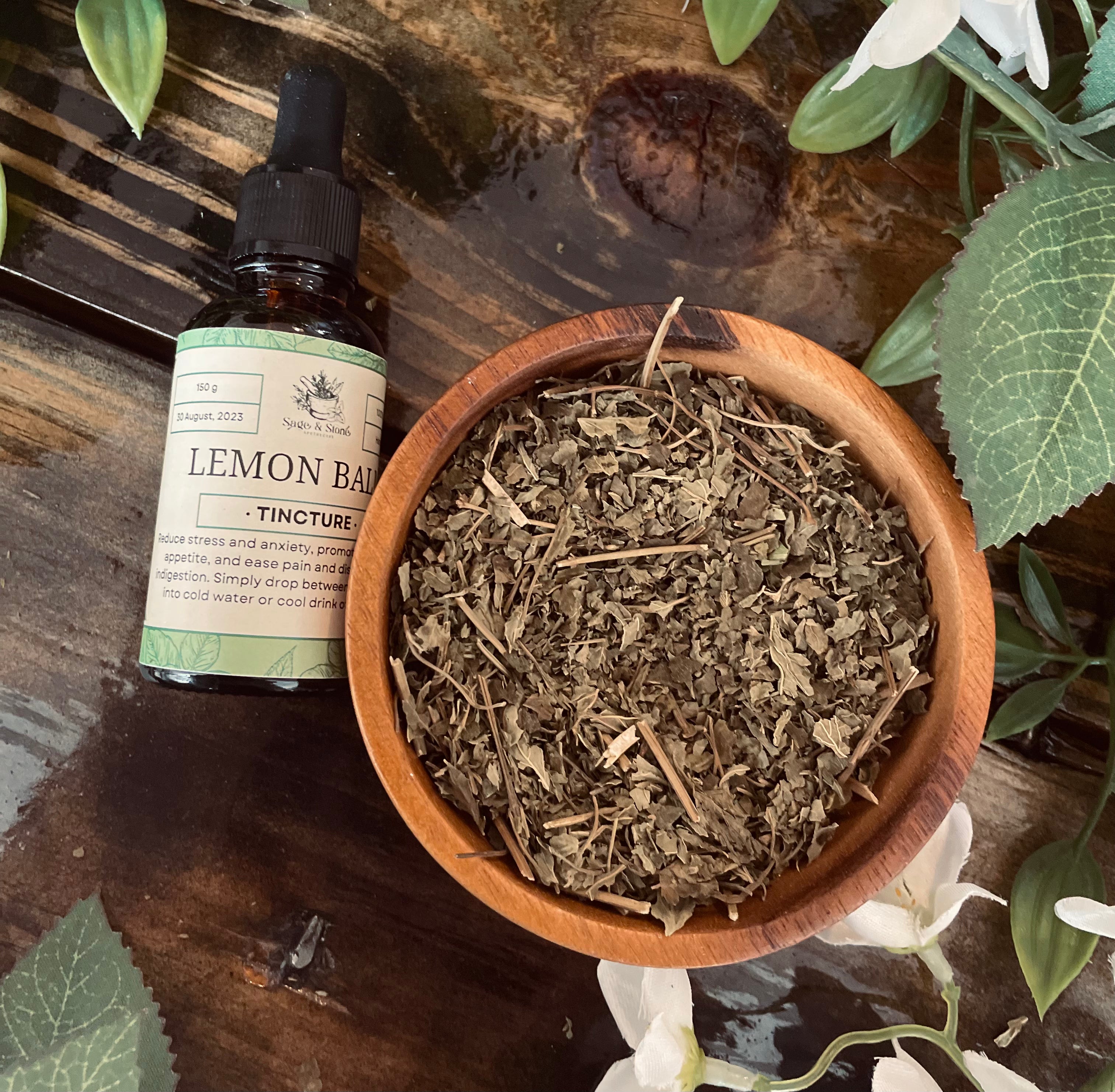 Lemon balm tincture in a glass bottle from Sage & Stone Apothecary, with a dropper cap and fresh lemon balm leaves nearby.