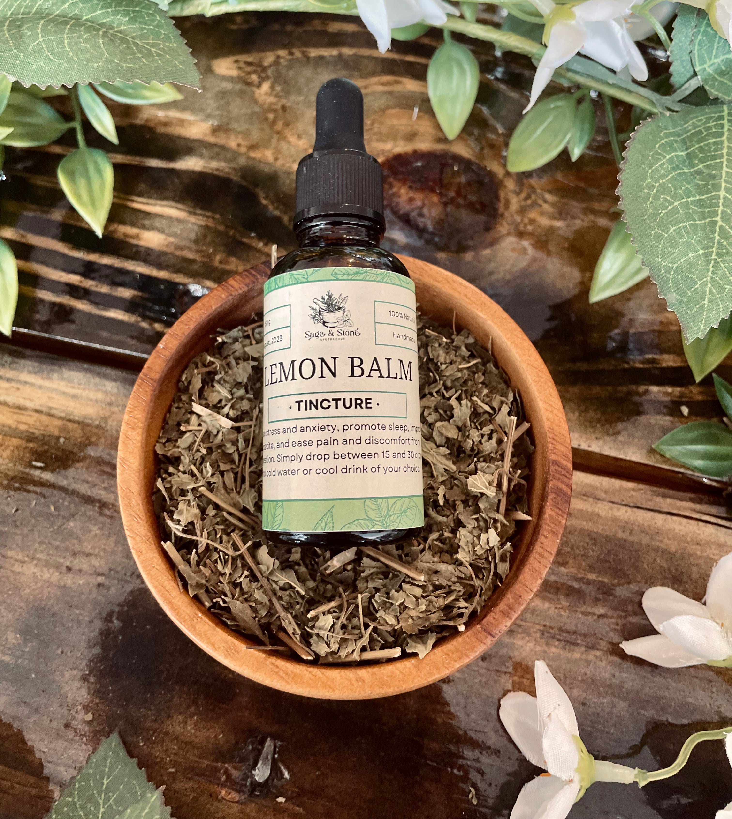 Lemon balm tincture in a 1 oz bottle from Sage & Stone Apothecary, with a dropper and fresh lemon balm leaves nearby.