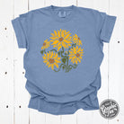 Comfort Colors She Blooms in Sunshine washed denim short sleeve graphic tee by The Graphic Tee, featuring a vibrant floral design.