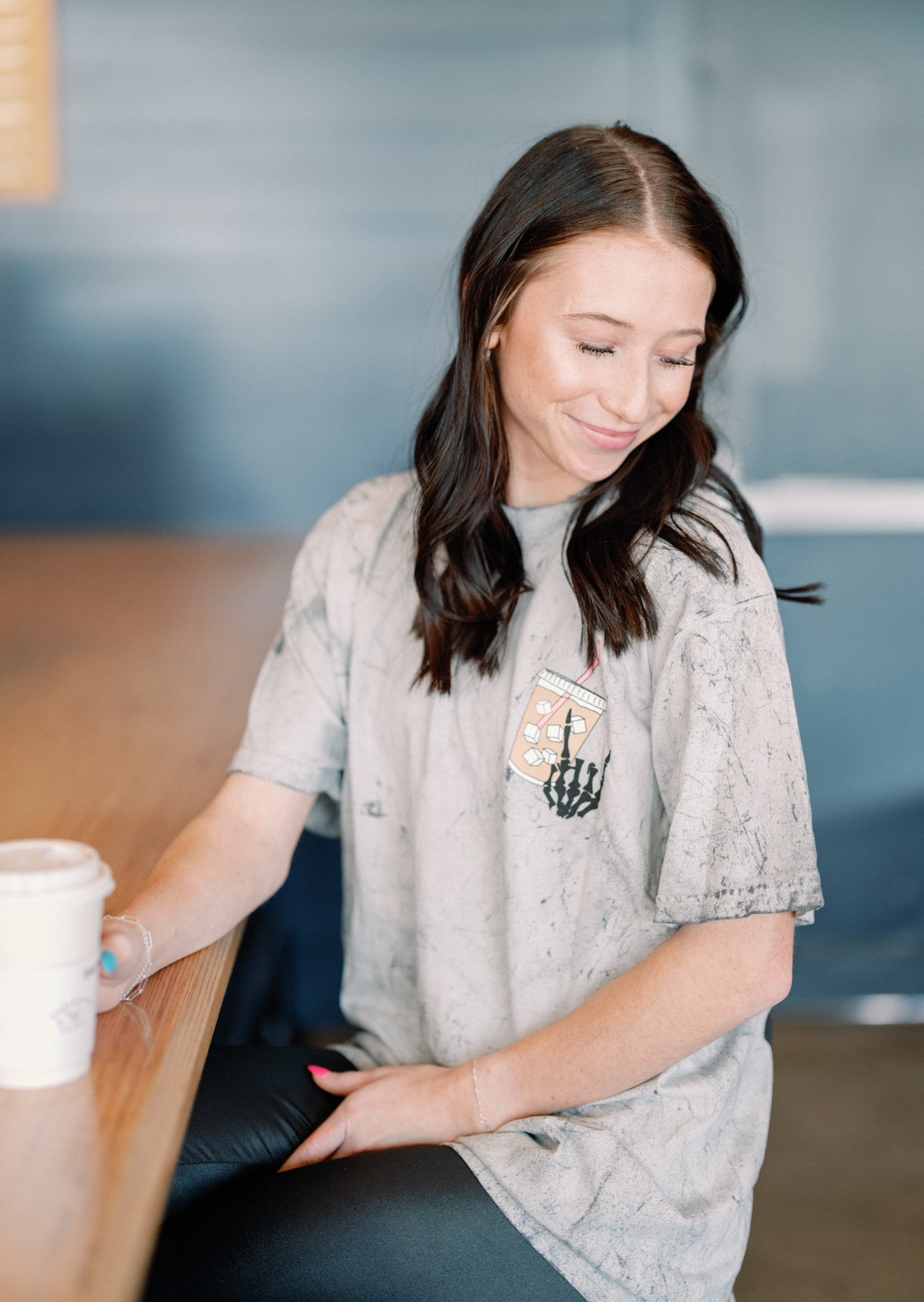 Gray graphic sweatshirt featuring "Fueled by iced coffee and anxiety" text, casual style, worn by a person with hands on hips.