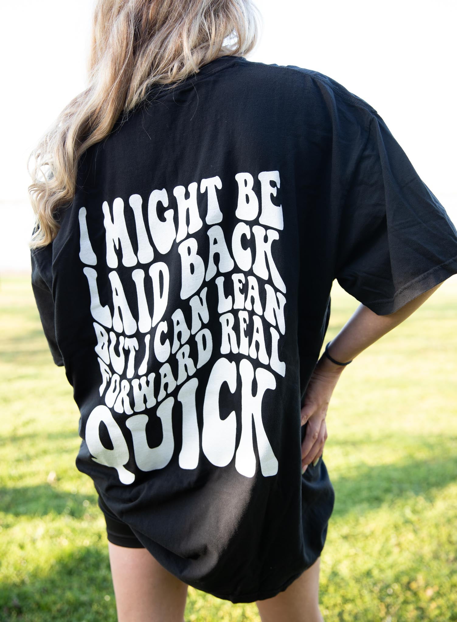 Black graphic tee by Shop Karma Tees with "I Might Be Laid Back" slogan and casual fit, displayed on a hanger.