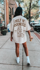Graphic T-shirt featuring "Milf and Cookies" design by Shop Karma Tees, with bold text and playful style on a casual cotton tee.