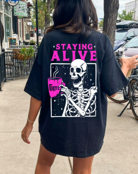 Black graphic T-shirt from Shop Karma Tees with "Staying Alive" design, casual fit, and vibrant print on the front.