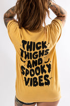 Black graphic tee from Shop Karma Tees featuring bold "Thick Thighs and Spooky Vibes" design on the front.