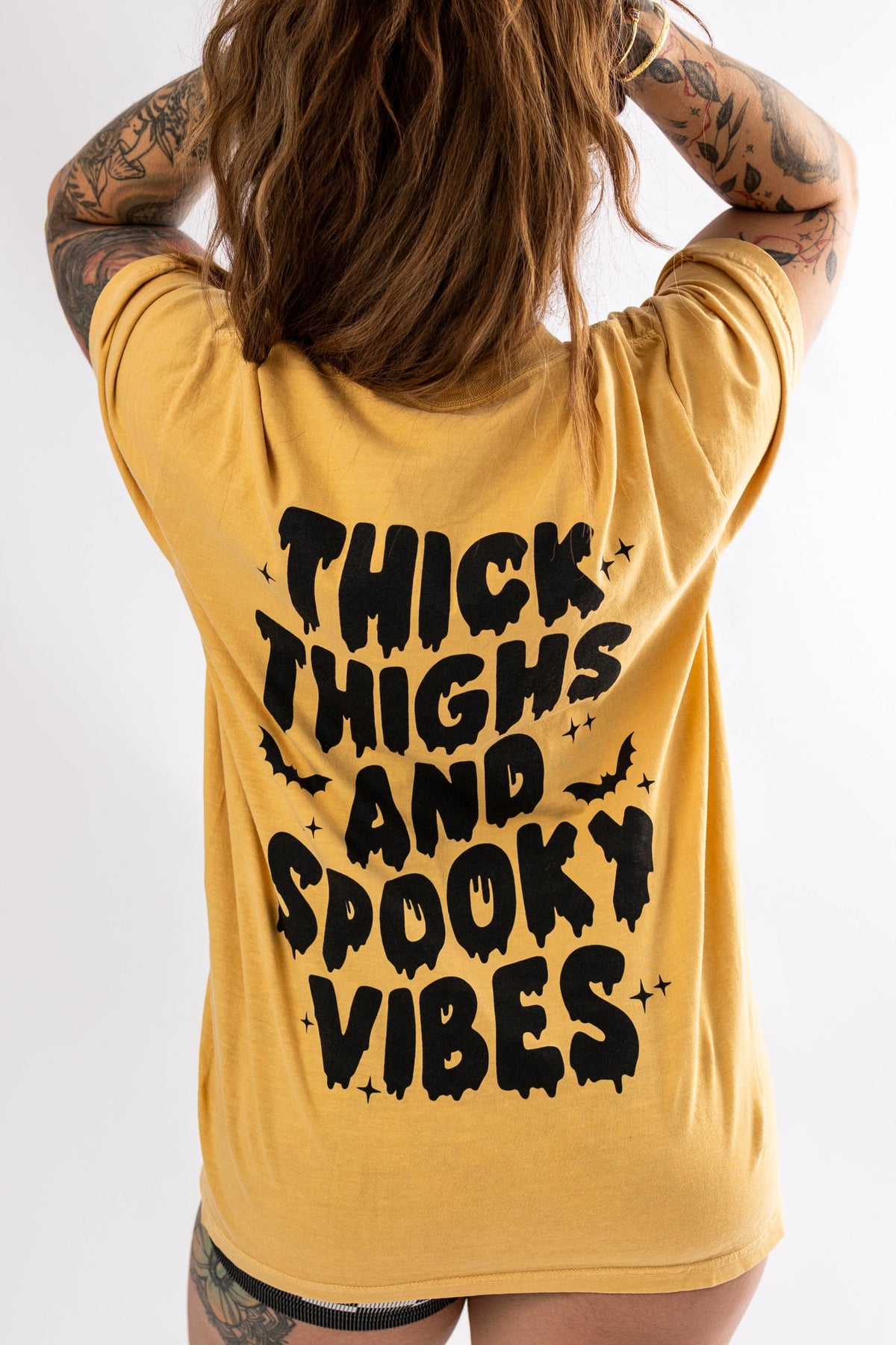 Black graphic tee from Shop Karma Tees featuring bold "Thick Thighs and Spooky Vibes" design on the front.