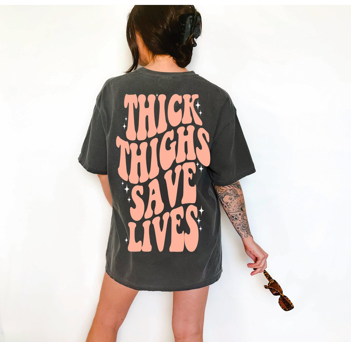 Thick Thighs Save Lives graphic T-shirt by Shop Karma Tees featuring a bold design on a casual cotton tee.