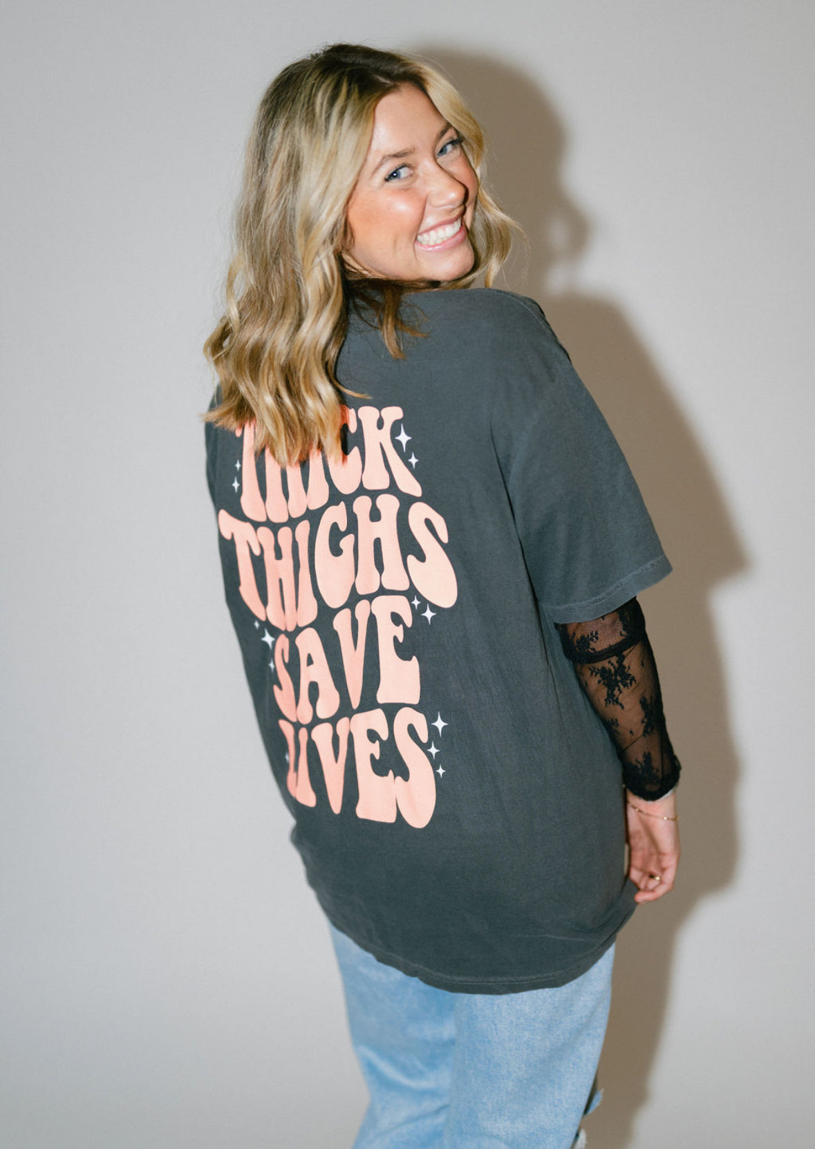 Black graphic T-shirt from Shop Karma Tees featuring bold "Thick Thighs Save Lives" text on the front.