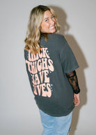 Black graphic T-shirt from Shop Karma Tees featuring bold "Thick Thighs Save Lives" text on the front.