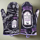 Pair of purple and black kitchen witch oven mitts with herb designs from Spirit Nest, perfect for baking and cooking.