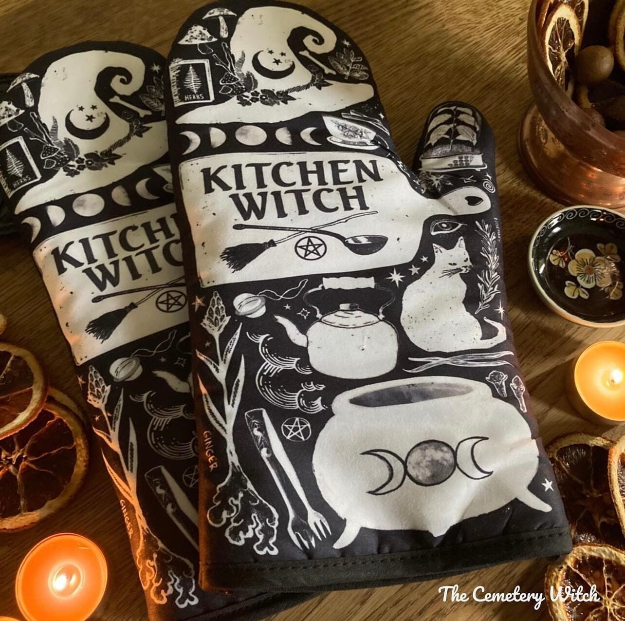 Purple and black witch-themed oven mitt set from Spirit Nest with herbs, featuring a kitchen witch design and comfortable fabric.