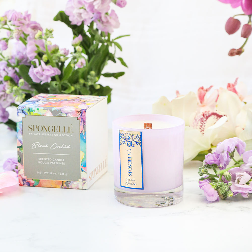Black Orchid Private Reserve Candle by Spongellé, a luxurious home fragrance in a sleek black container with a flickering flame.