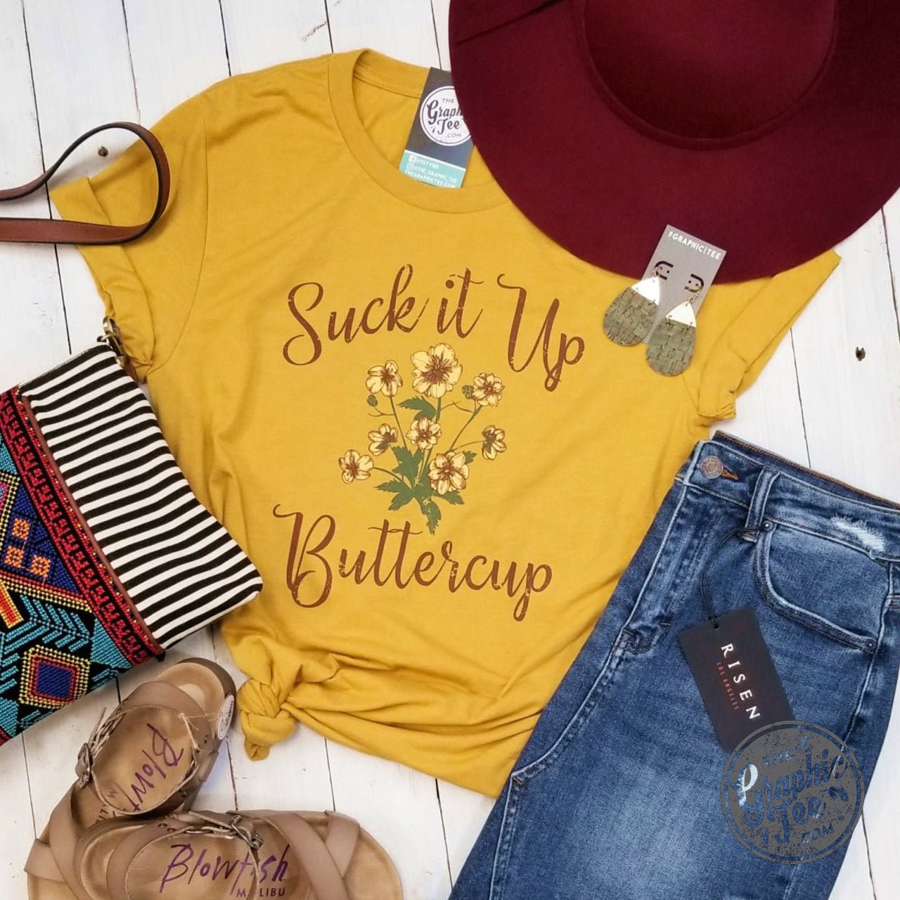Unisex graphic tee by The Graphic Tee with "Suck It Up Buttercup" slogan in bold black text on a white T-shirt.