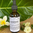Bottle of Sweet ʻŌkole Soap Rosemary Hair & Scalp Oil with rosemary sprigs and a dropper on a neutral background.