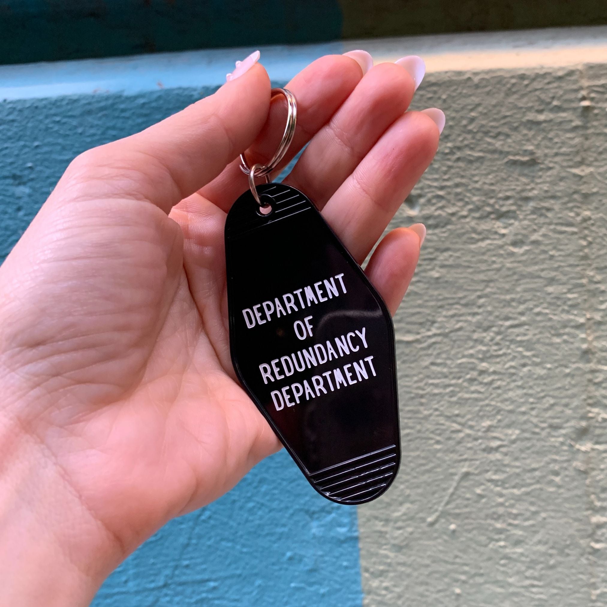 Black Motel Style keychain featuring the Department of Redundancy Department logo, made by The Bullish Store.
