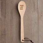 Wooden cooking spoon with "Peace Love Bake" engraving in muslin gift bag, perfect for kitchen utensils and baking enthusiasts.
