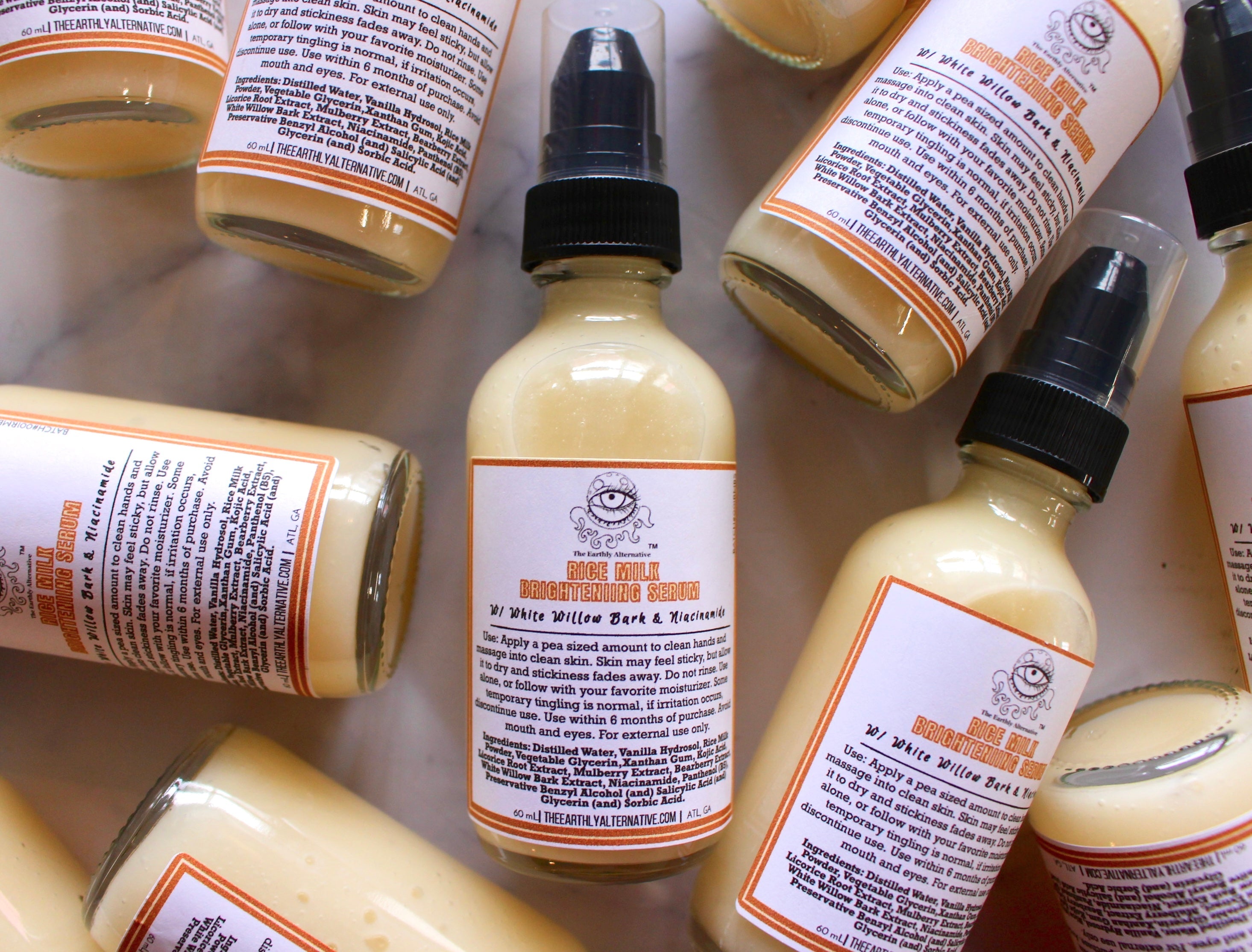 2 oz bottle of The Earthly Alternative Rice Milk Brightening Serum, featuring a clear glass container with a white pump dispenser.