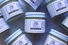 The Earthly Alternative beard balm jar with a natural label, showing a close-up of the product container and wooden background.