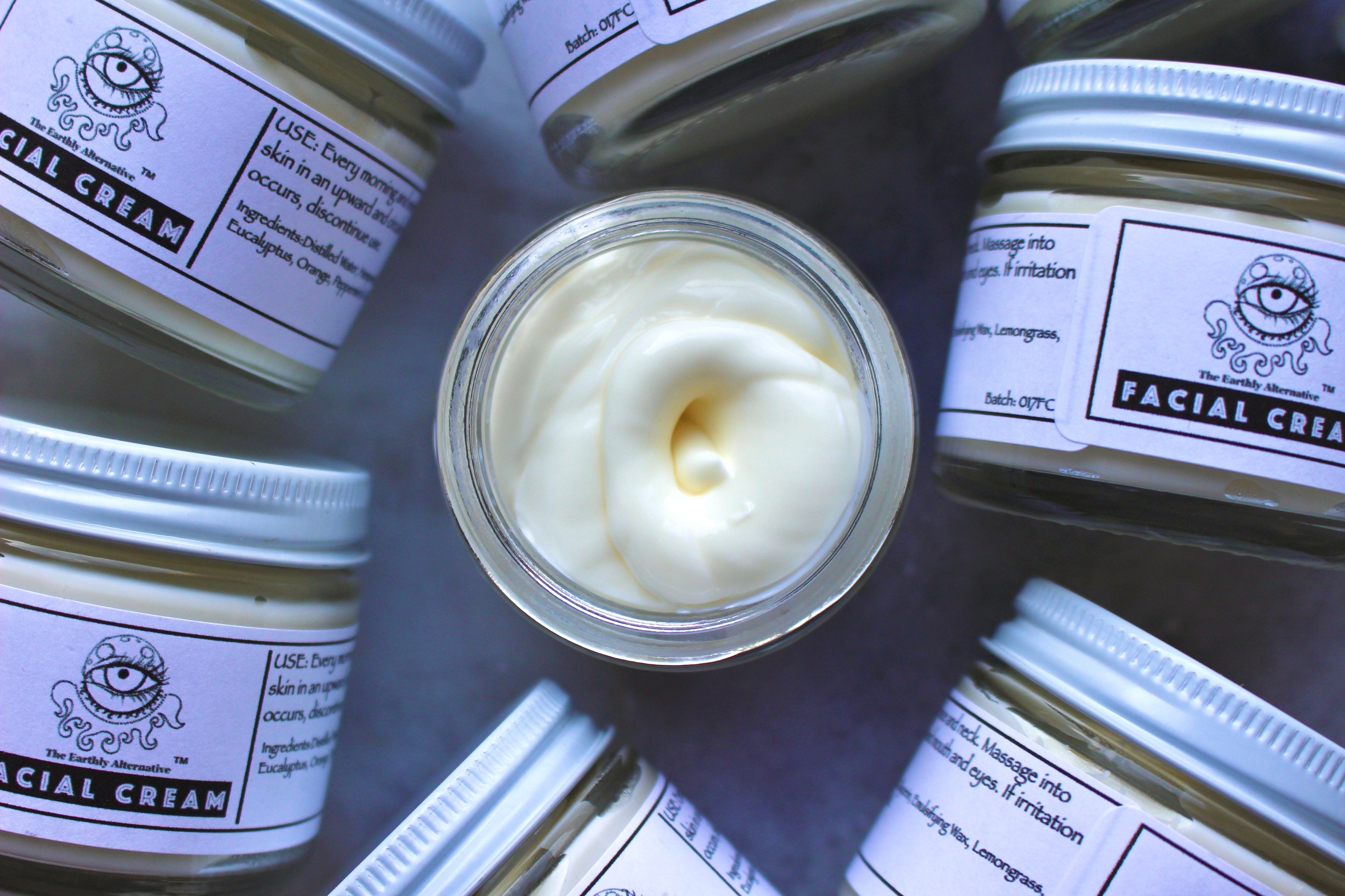 Cream jar labeled "Facial Cream" from The Earthly Alternative, showing a close-up of the skincare product with a smooth, creamy texture.