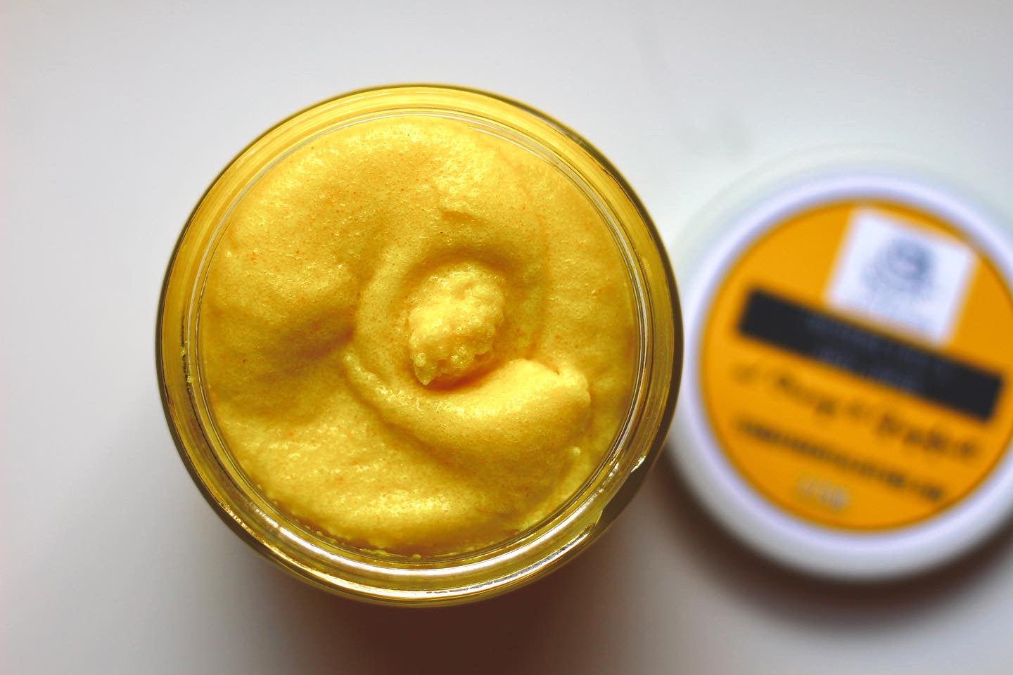 Natural turmeric face and body scrub by The Earthly Alternative, showing a jar of golden exfoliating scrub with turmeric roots.