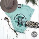The Graphic Tee Tick Me Off Again Heifer Short Sleeve Heather Prism Mint graphic T-shirt showing a humorous design on the front.