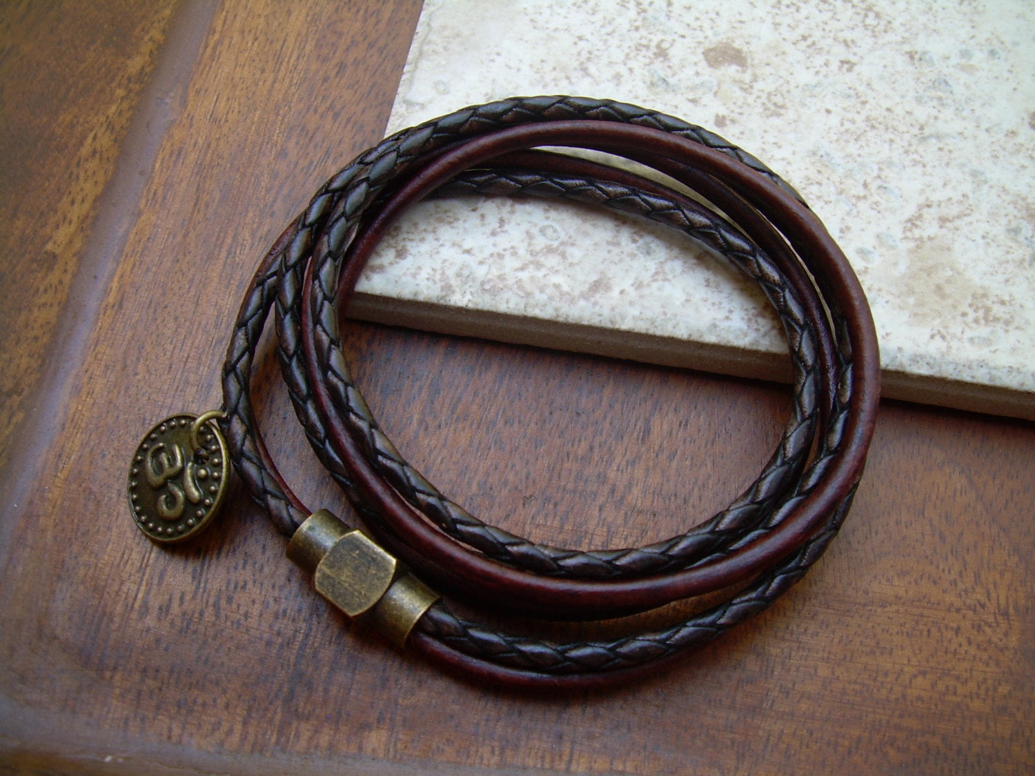 Dark brown leather bracelet with Om charm and antique brass magnetic clasp, featuring a triple wrap design for a stylish look.