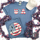American flag smiley face graphic T-shirt by The Graphic Tee, short sleeve comfort wash tee with patriotic design.