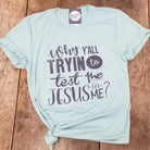 Dusty blue graphic t-shirt from The Graphic Tee featuring the phrase "Why Y'all Tryin to Test the Jesus in Me" in bold text.