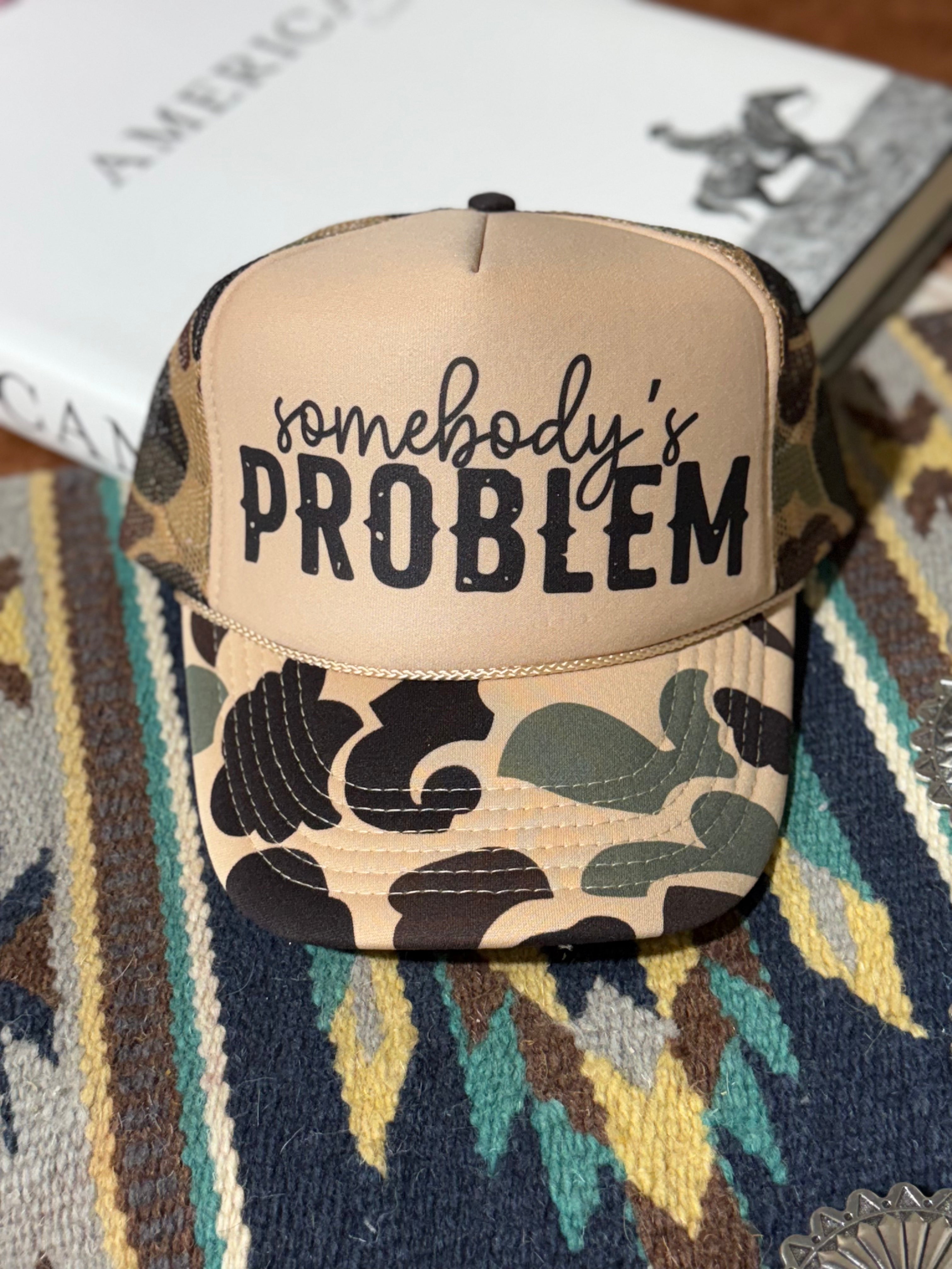 Wild Junkie Somebody's Problem camo trucker hat with mesh back and curved brim, featuring a bold embroidered design.